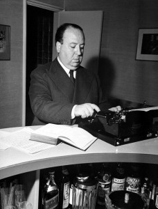 Alfred Hitchcock standing at a typewriter