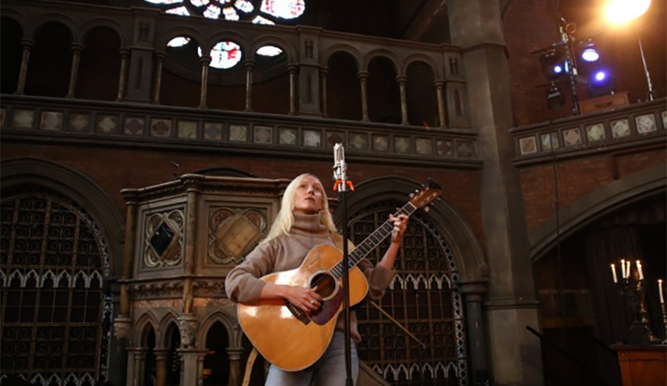 Singer songwriter, Laura Marling wearing a cream polo neck jumper and jeans and strumming a guitar at Union Chapel.