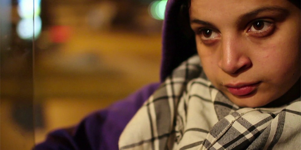 Close up of a young Arab female activist wearing a purple hoodie and black and white scarf.