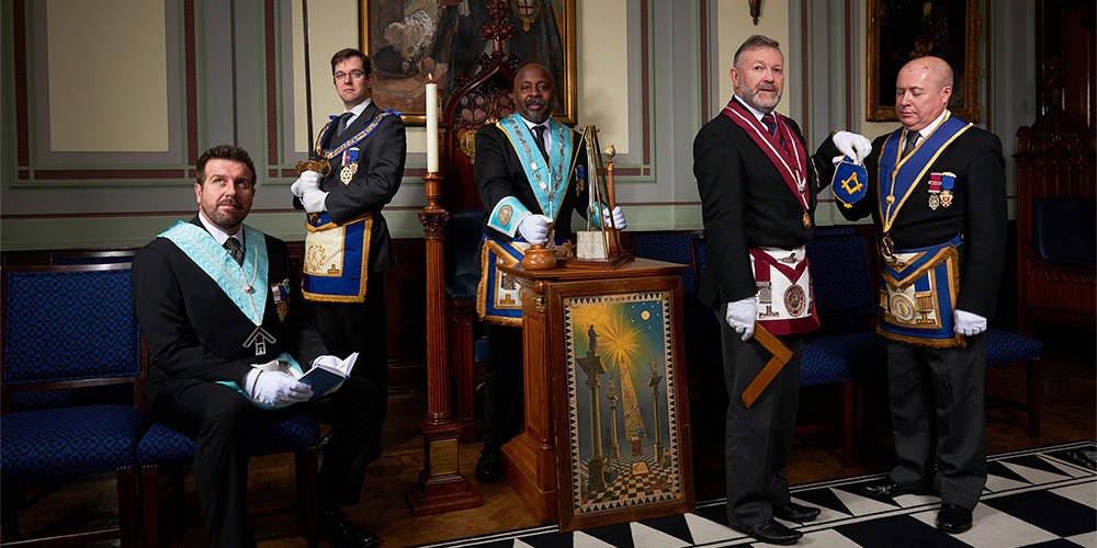 Five freemasons dressed in full regalia and holding Masonic artefacts