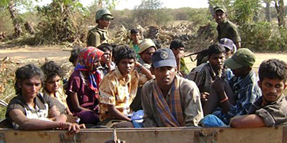 A disturbing picture of a group of young Tamils sitting at the back of a truck with Sri Lanka soldiers holding guns.