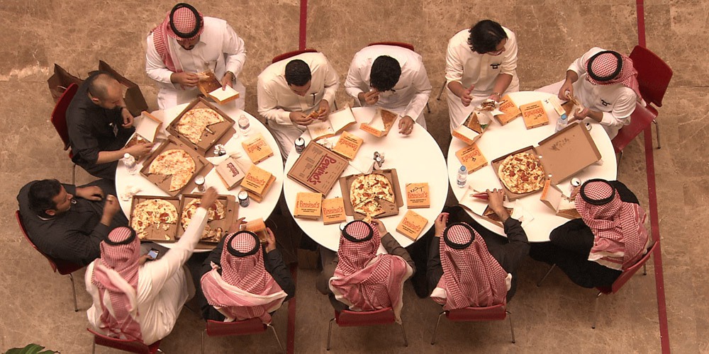 Overhead view of people eating pizza at three small circular tables