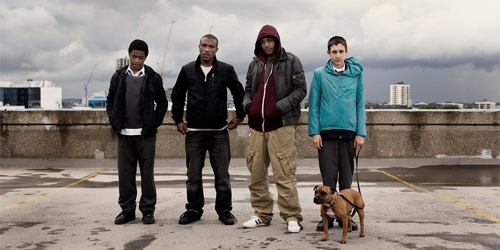Four Top Boy cast members including Ashley Walters and Kane Robinson on an urban rooftop with a dog