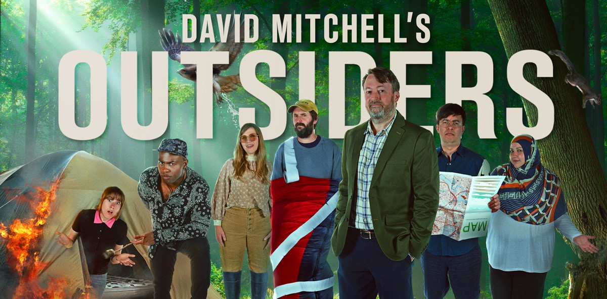 The cast of Outsiders season 2 standing in a forest including David Mitchell, Maisie Adam, Fatiha El-Ghorri, Darren Harriott, Jessica Hynes, Phil Wang and Joe Wilkinson.