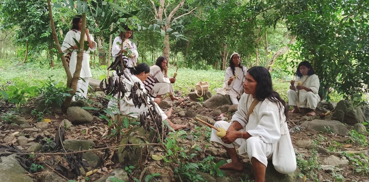 Seven members of the indigenous South American Kogi community sitting and standing in the forest of the Sierra Nevada de Santa Marta mountain range in Colombia.