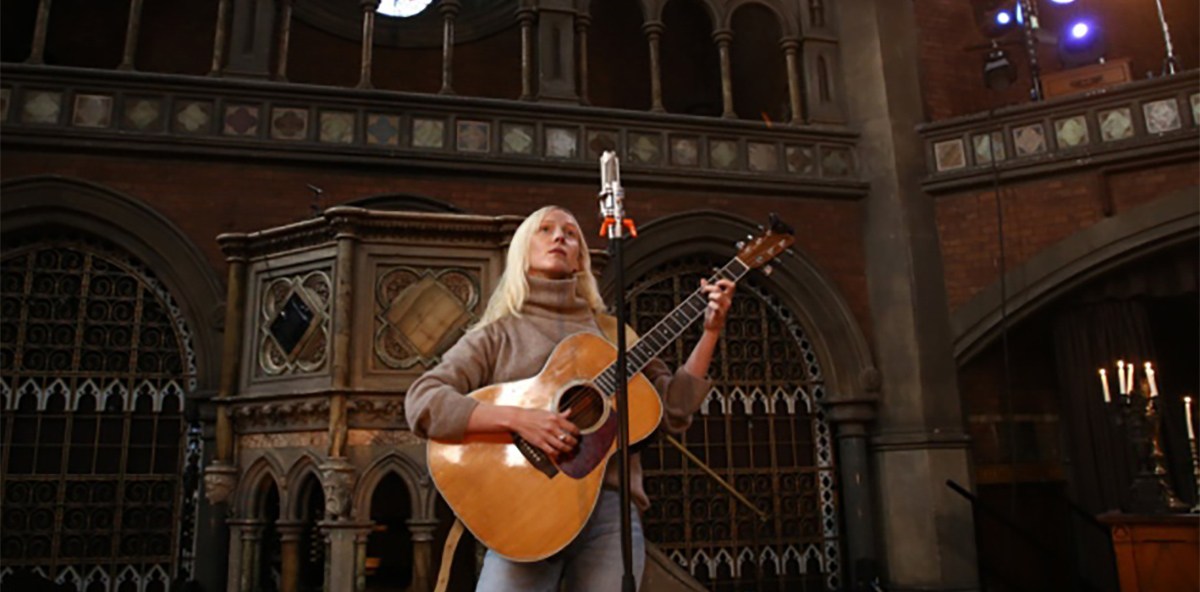 Singer Songwriter, Laura Marling, with long, straight blond hair, strumming guitar at Union Chapel main auditorium